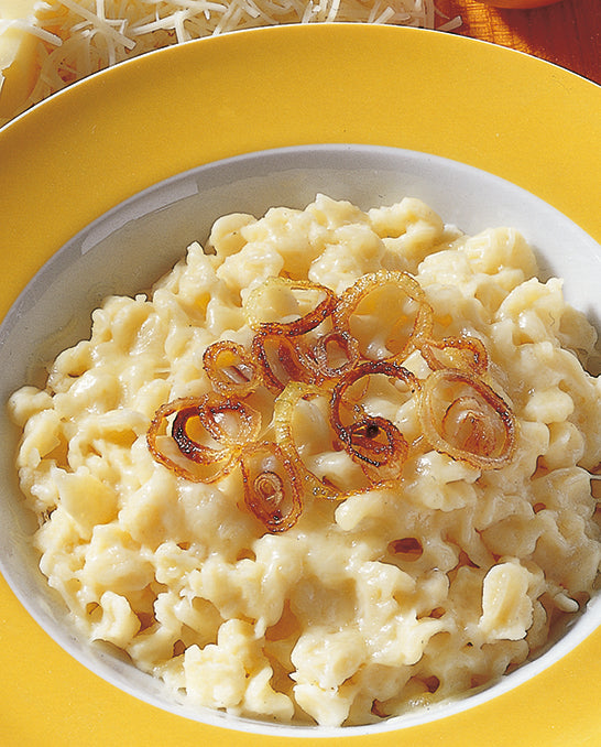 Frische Kässpätzle angerichtet auf einem gelben Tel-ler, garniert mit Zwiebelringen