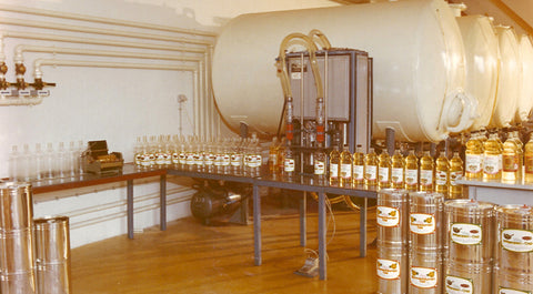 Filling machine where oil bottles were filled by hand and white storage tanks.
