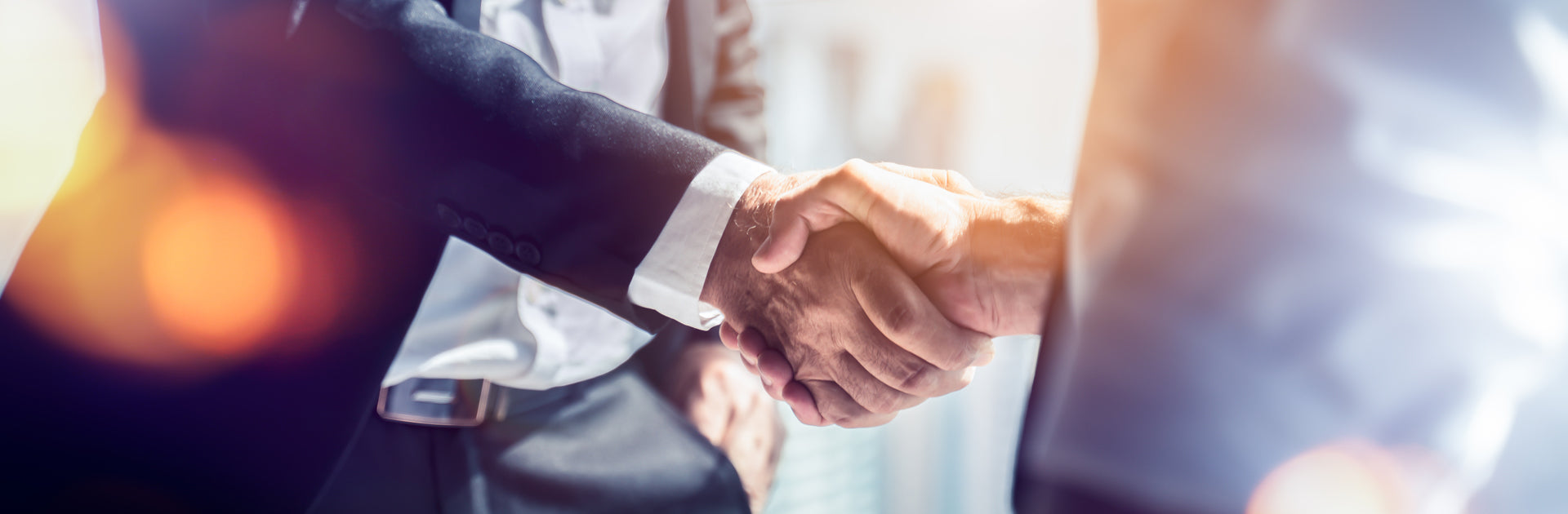 Two people are shaking hands. They are businessmen and it is a warm light in an office