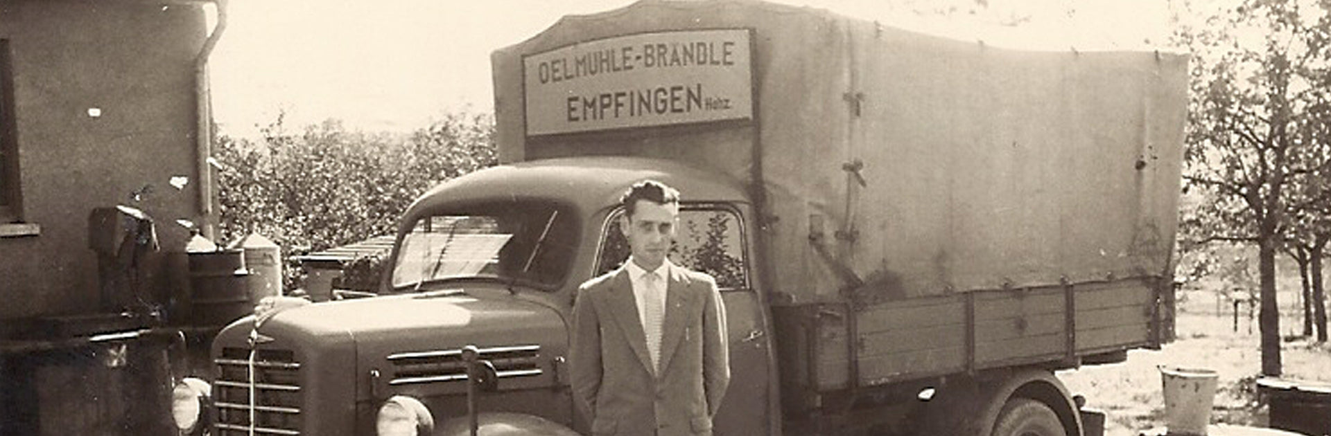 Pius Brändle steht als junger Mann vor einem LKW mit dem damals Ware ausgefahren wurde.
